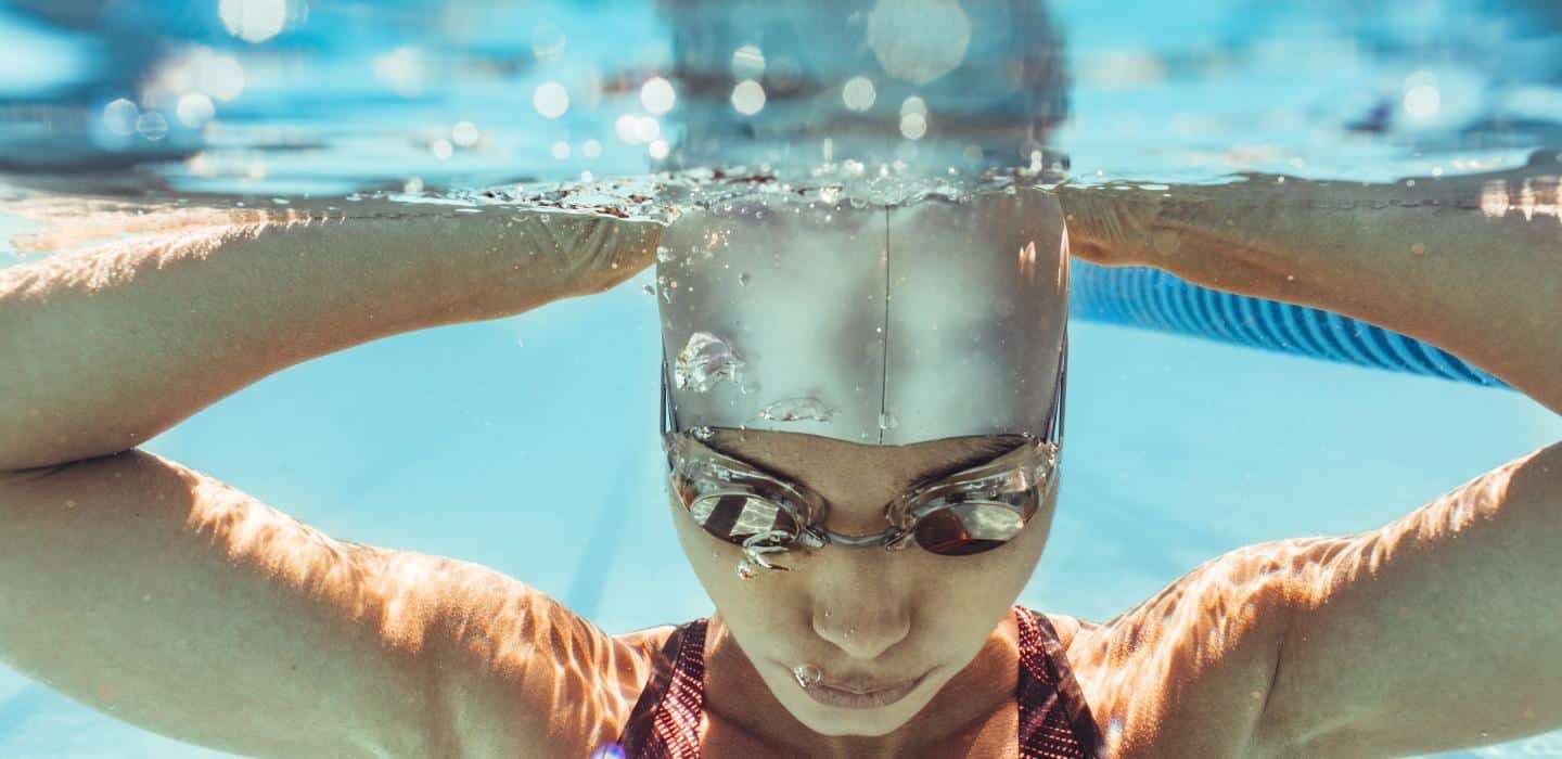 Underwater shot of a swimmer with a silver cap and goggles, arms extended to the sides as they prepare to dive.