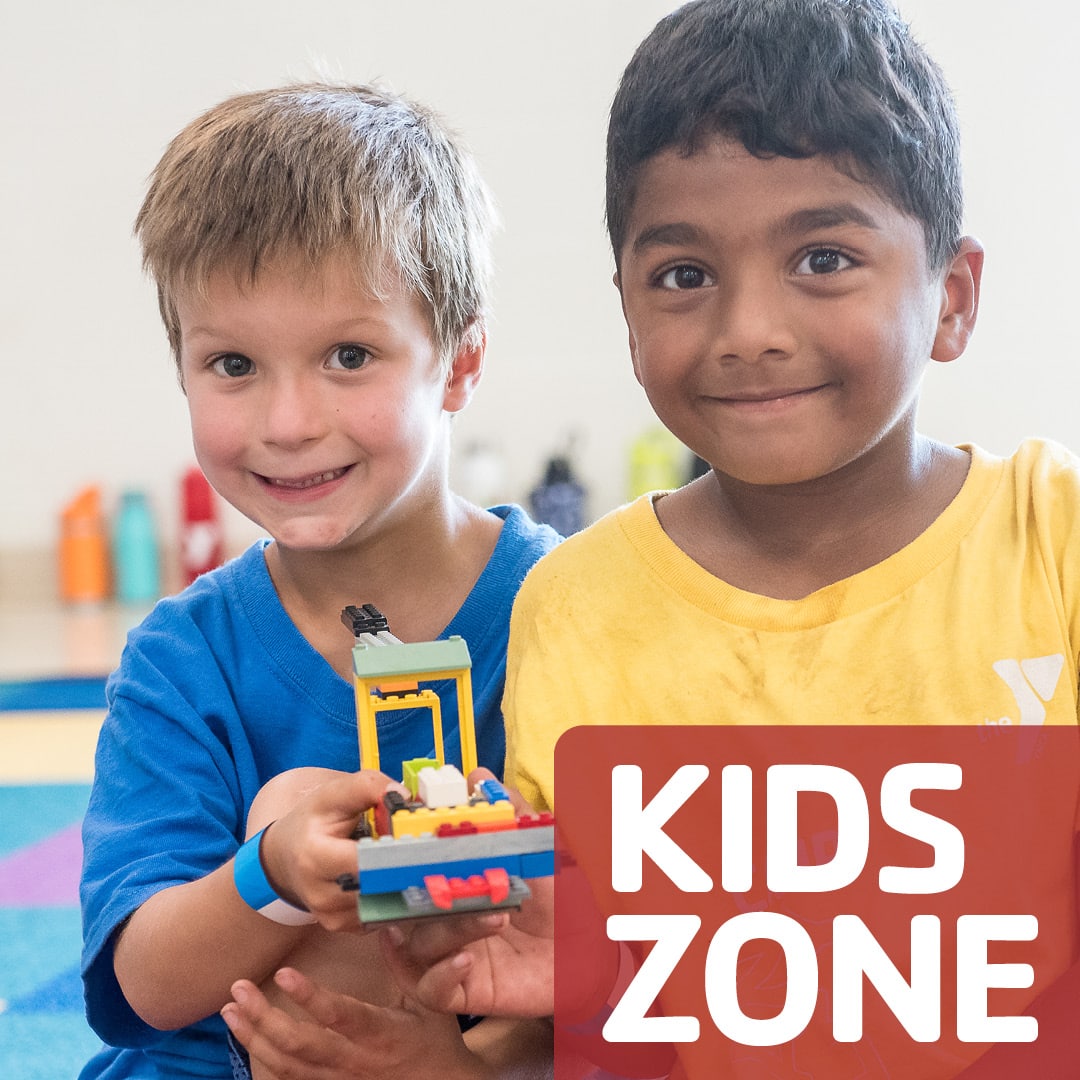 Two smiling kids hold a small LEGO build in a bright classroom, with a red 'KIDS ZONE' badge in the corner.